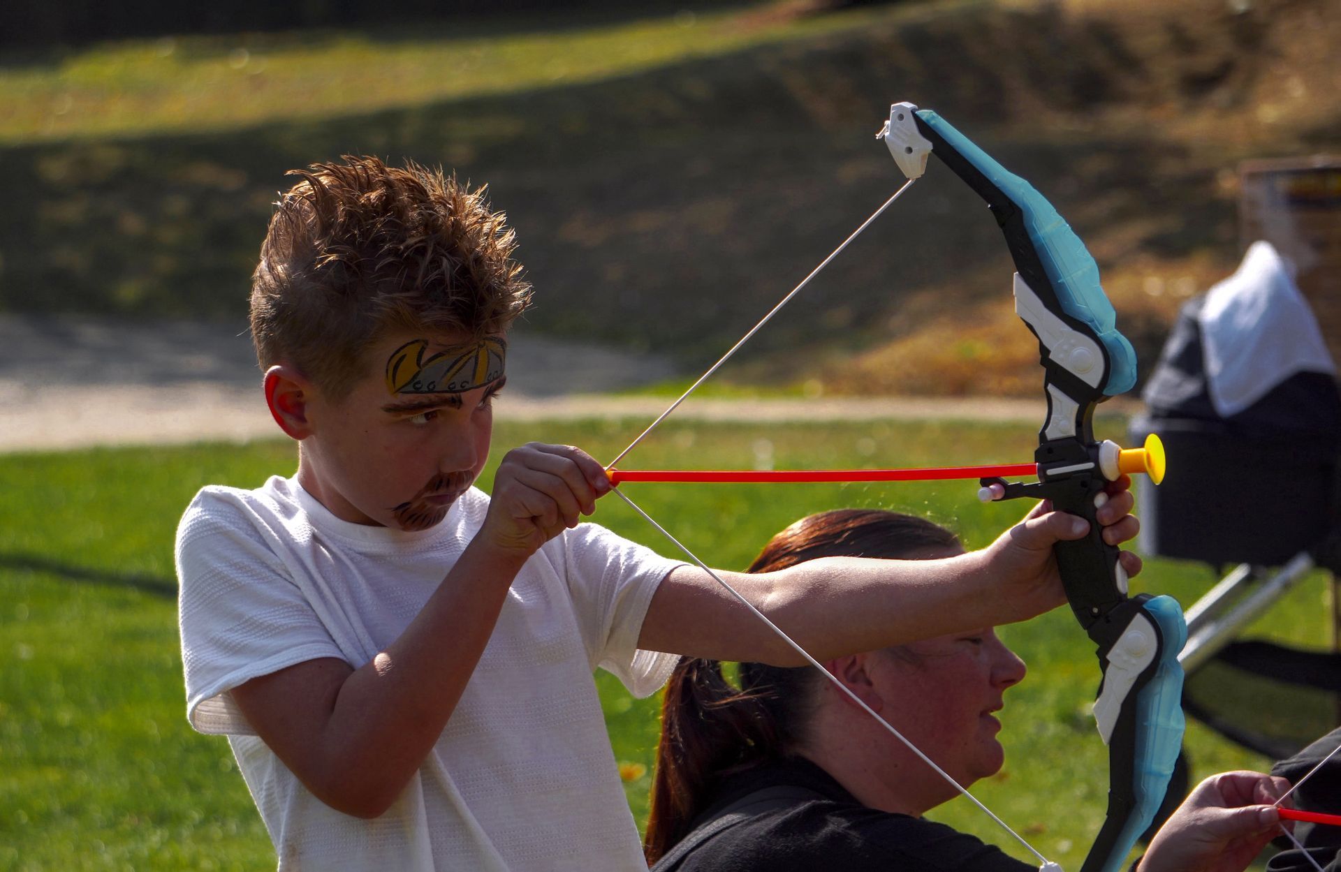 A young child using a plastic bow and arrow at an event.