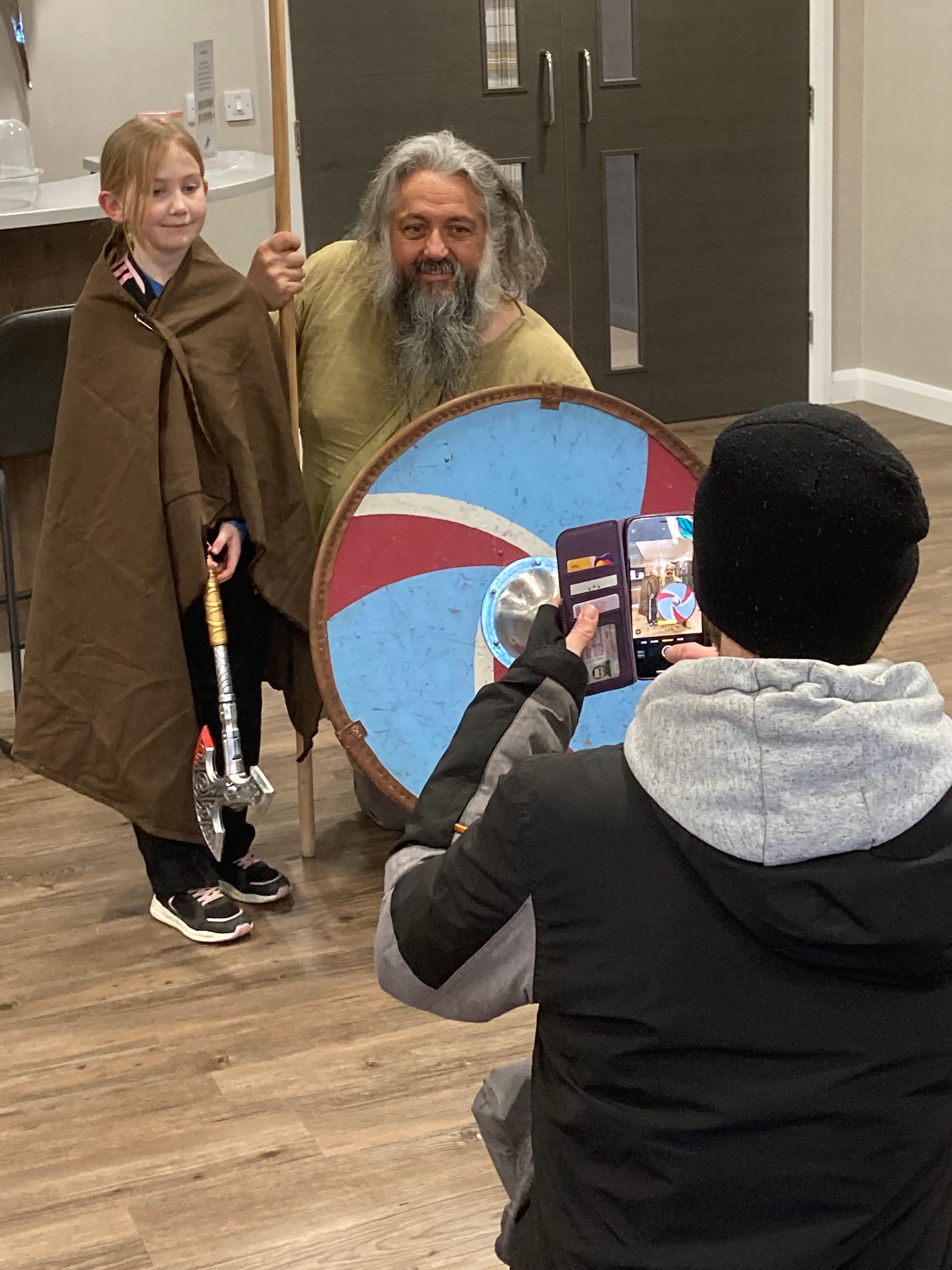 A man is taking a picture of a little girl and a man holding a shield.