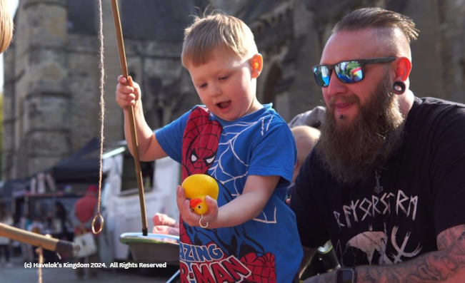 A man with a beard is holding a yellow rubber duck next to a little boy wearing a spiderman shirt.