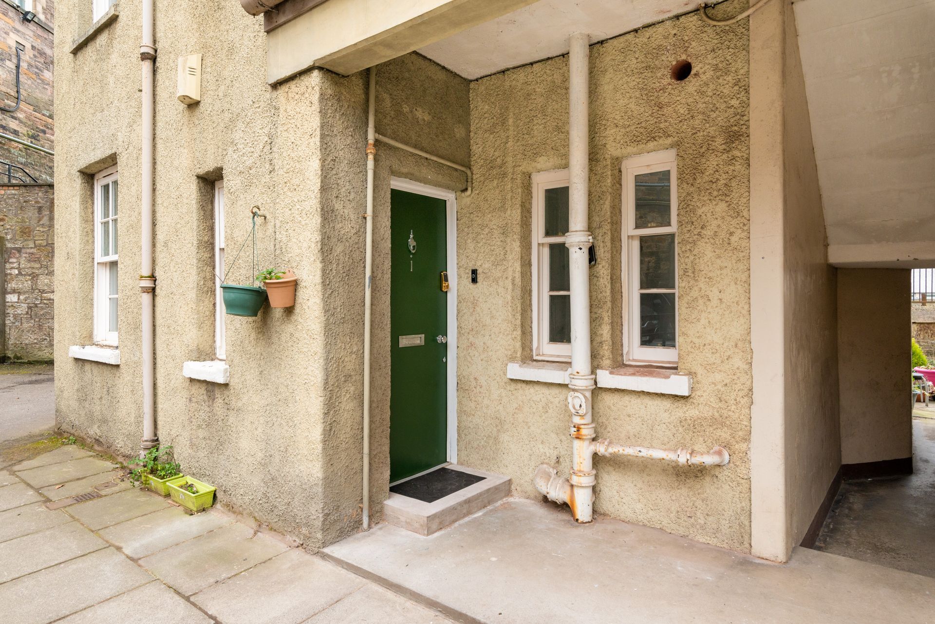 Exterior of a building with a green door. Beige stucco walls, windows, and potted plants. Paved walkway.