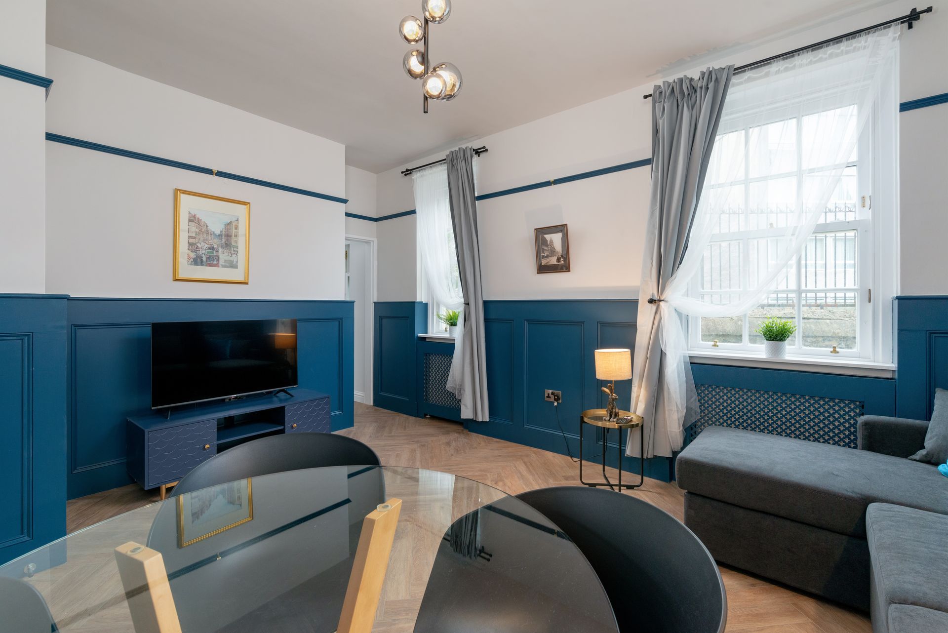 Living room with blue paneling, white walls, gray sofa, and a glass-top dining table.