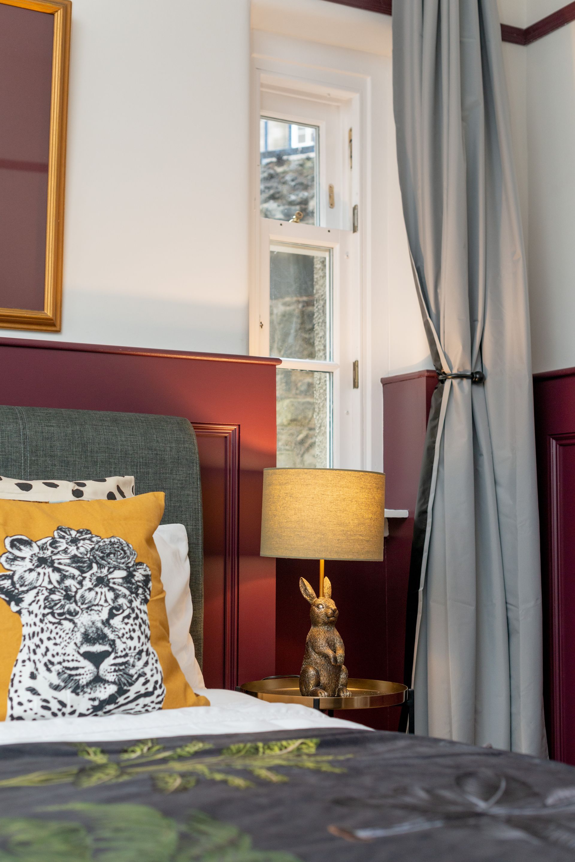 Bedroom with a leopard-print pillow, gold bunny lamp, window, and burgundy accent wall.