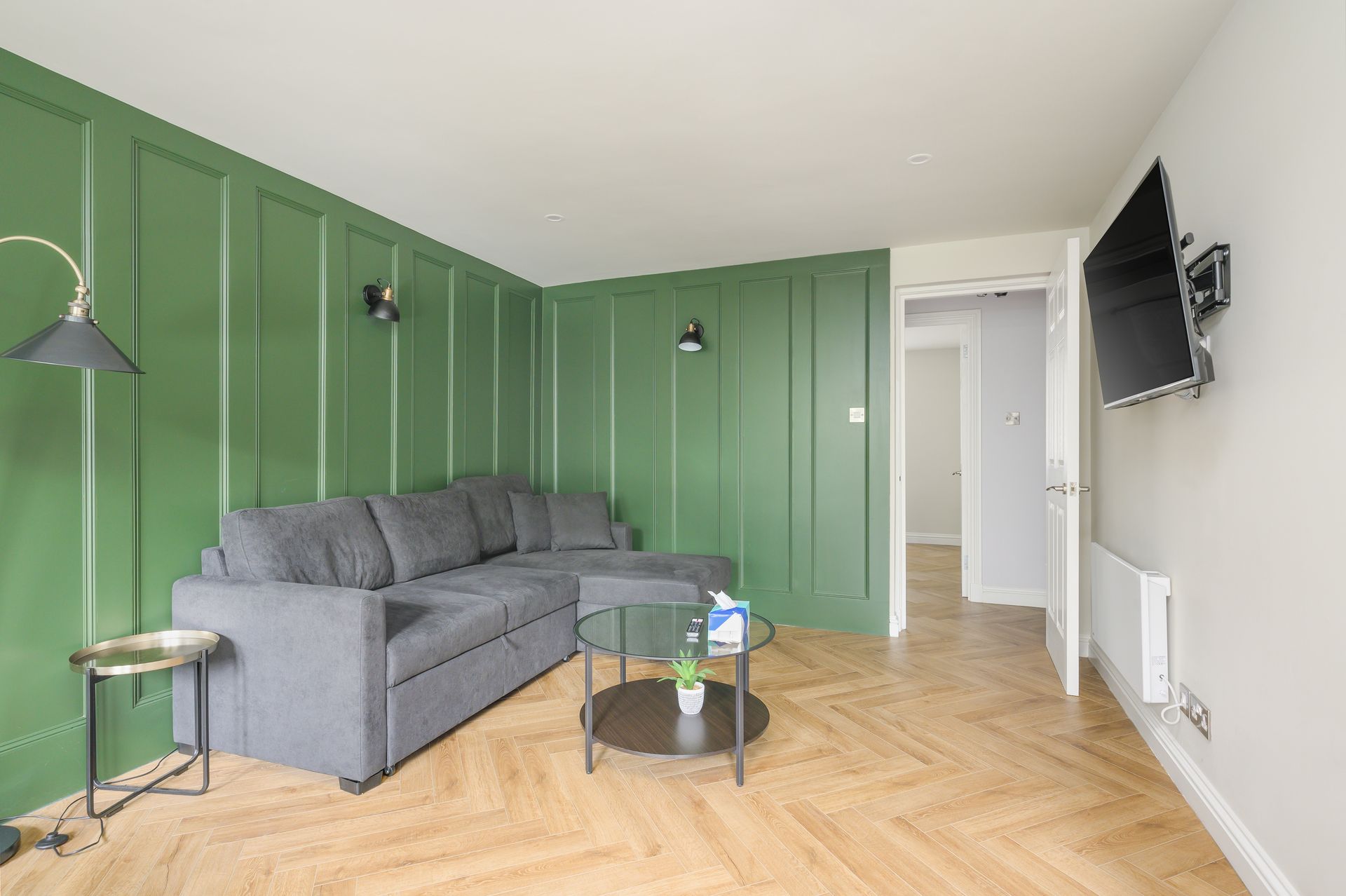 Living room with green accent wall, gray sofa, TV, and wooden floor.