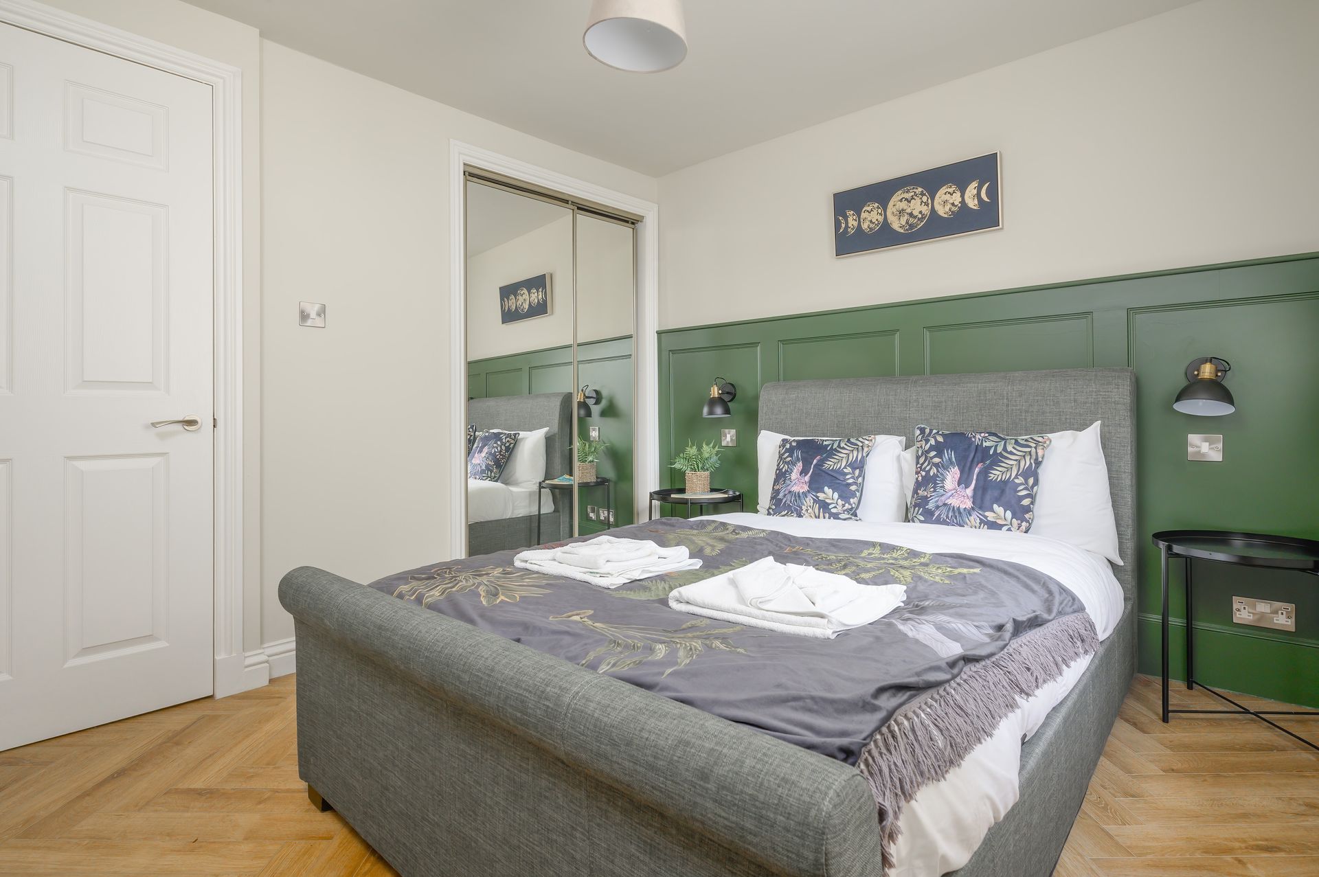 Bedroom with green paneled wall, gray bed, mirrored closet, and wooden floor.