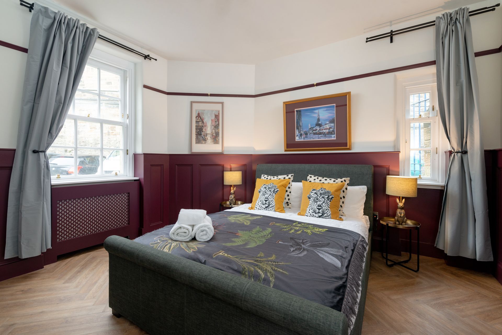Bedroom with bed, windows, and two bedside tables. Burgundy and white walls, grey curtains.