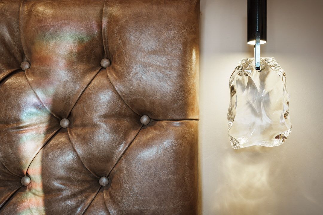 Tufted brown leather headboard with a hanging, illuminated crystal pendant.