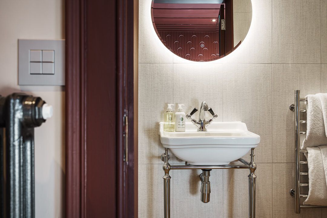 Bathroom with a small white sink, round mirror, and towel warmer.