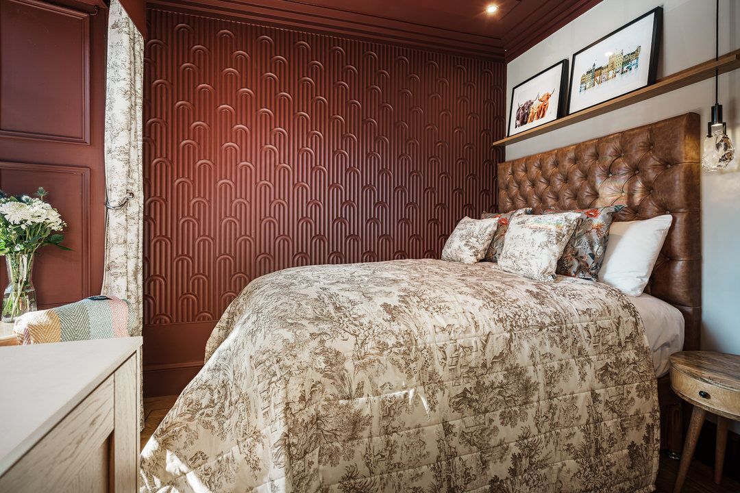 Cozy bedroom with burgundy walls, bed with floral comforter, headboard, small wooden table.