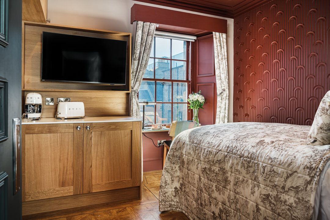 Bedroom with bed, window, TV, and wooden cabinet, with red and cream tones.