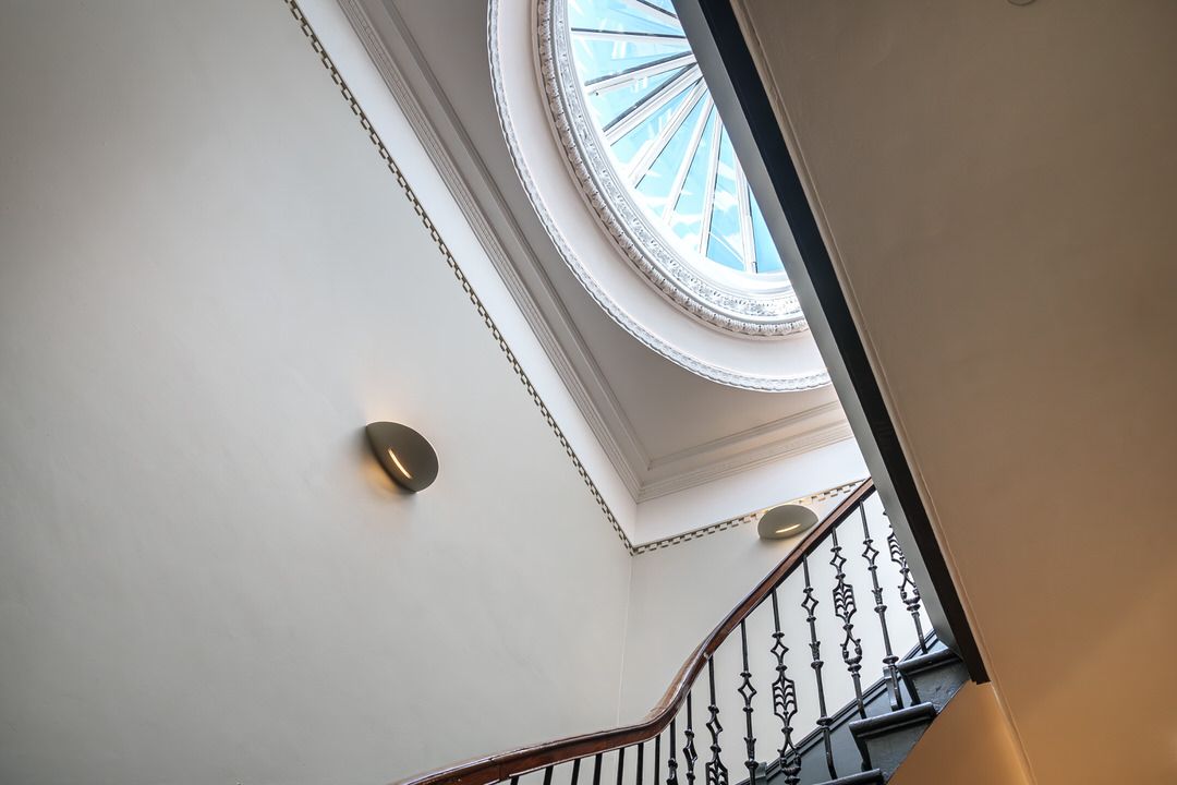 Stairwell with curved staircase leading up to an ornate ceiling with a round skylight.