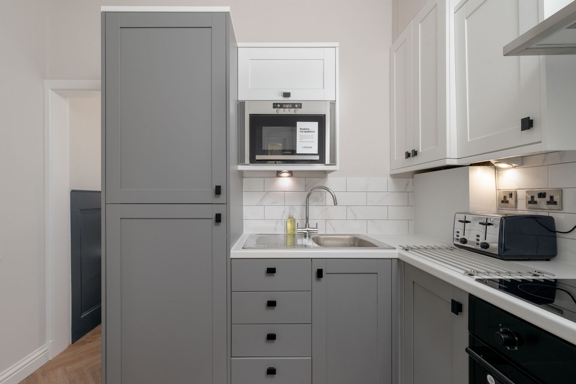 Small, modern kitchen with gray cabinets, white backsplash, microwave, and sink.