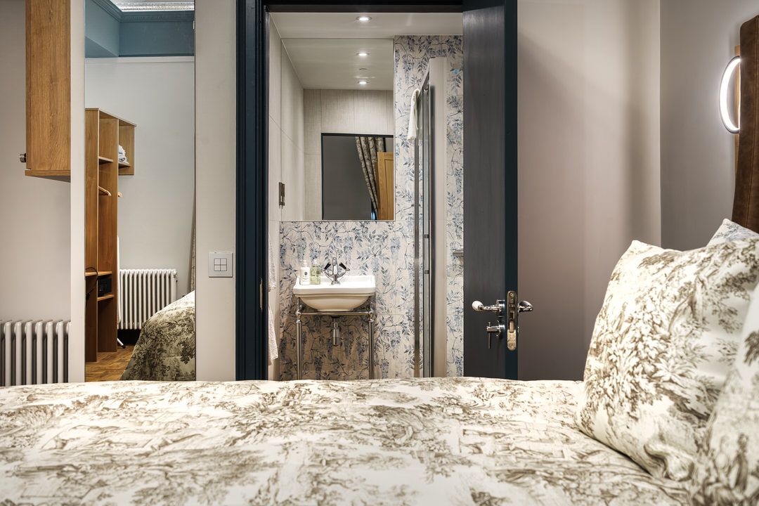 Bedroom interior with view into a bathroom. The bed has floral pattern bedding. Bathroom features marble finishes.