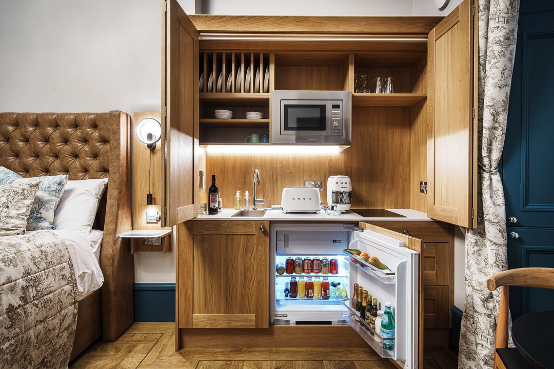 Compact hotel room kitchenette with microwave, refrigerator, and sink. Wooden cabinets.