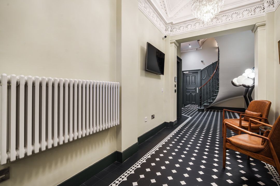 Long hallway with radiator, TV, seating, and patterned floor.