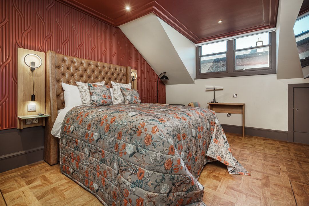 Bedroom with floral bedding, tufted headboard, red walls, and wooden floors.