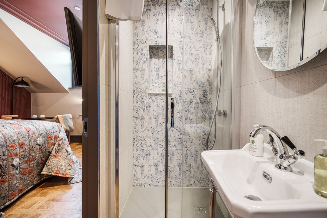 Bathroom with glass shower, sink, and partial view of bedroom with floral bedding.