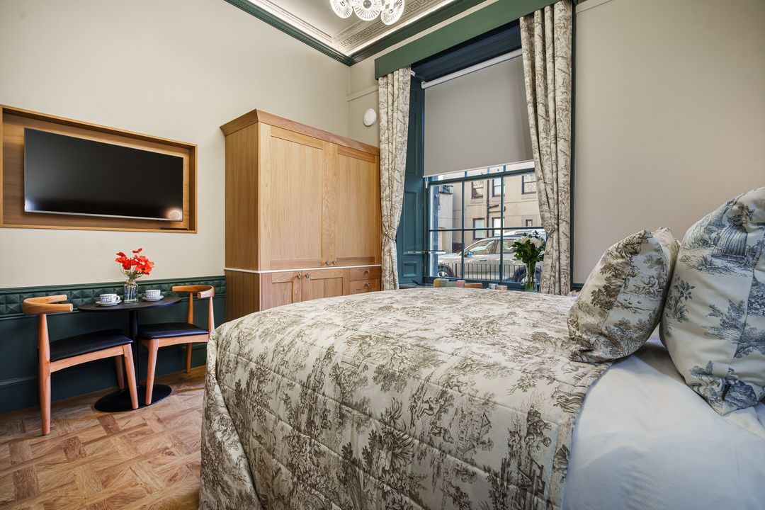Cozy hotel room with a bed, table, TV, wardrobe, and window with curtains.