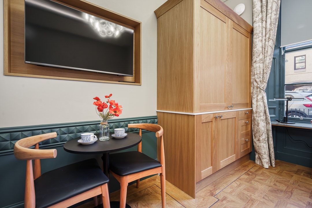 Small room with table, chairs, TV, and cabinet. Red flowers in vase on table.