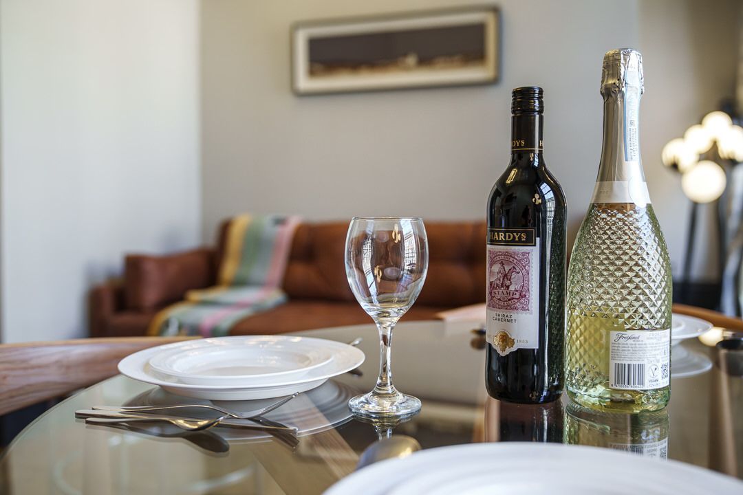 Table set with wine, champagne, glasses, and plates; a couch and art piece are in the background.