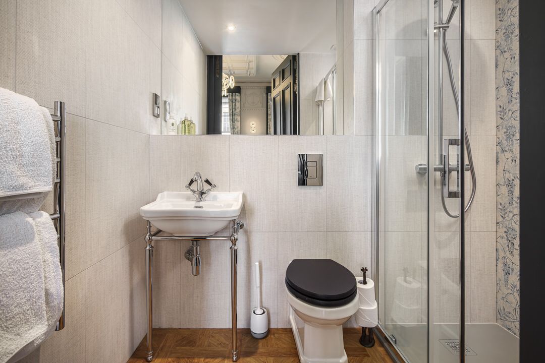 Small bathroom with a white sink, toilet, and shower. A towel rack is on the left.