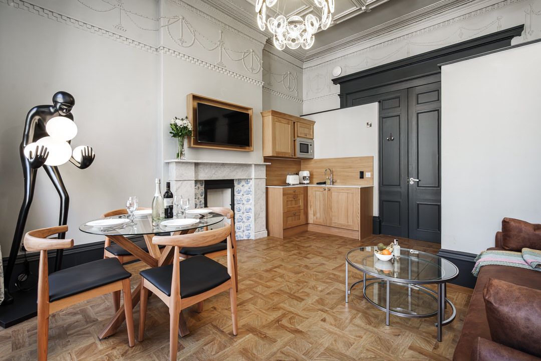 Living room with dining table, kitchenette, and artwork, including a tall black lamp and a chandelier.