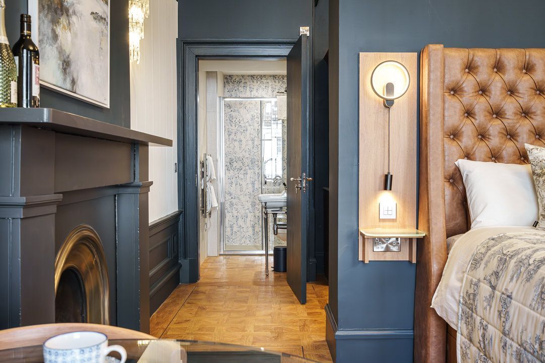 Bedroom with dark blue walls, fireplace, open doorway to bathroom, and bed with tufted headboard.