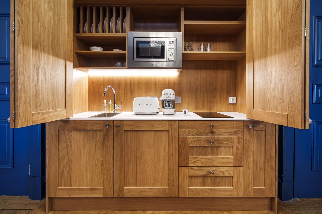 Wooden kitchenette with microwave, sink, toaster, and small appliances. Doors open.