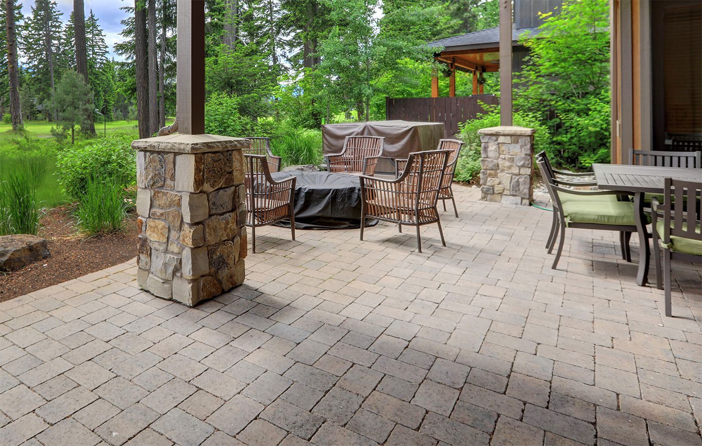 Patio with stone pavers, wicker chairs, table, and grill beside a wooded backyard