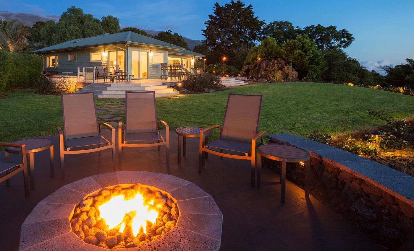 Fire pit with chairs on a patio overlooking a lit house at dusk
