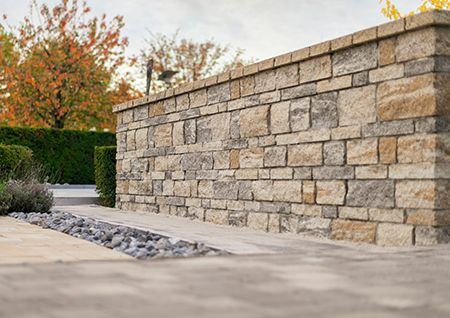 Stone retaining wall beside a paved path and landscaped shrubs in a quiet outdoor garden area