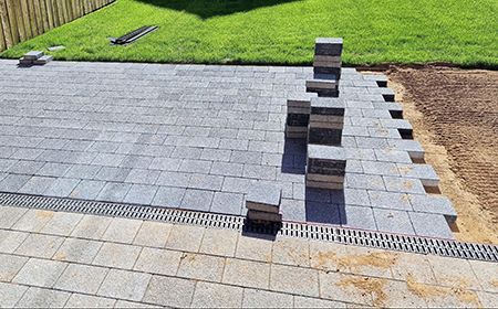 Stacked gray pavers beside a newly laid stone patio edge and lawn
