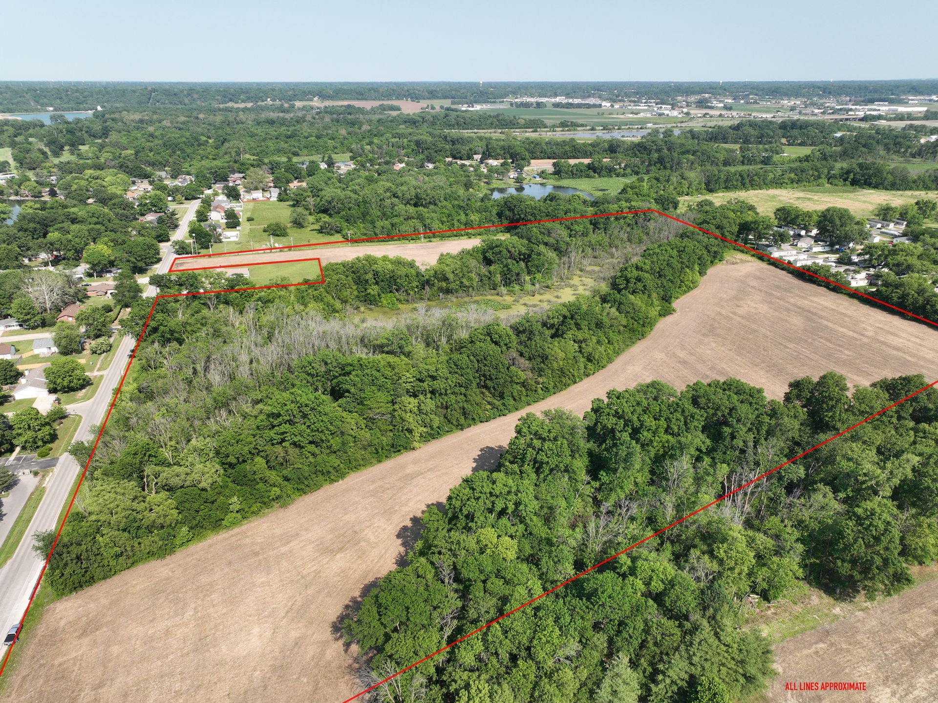Aerial view of a wooded lot beside fields and a road on a clear day.