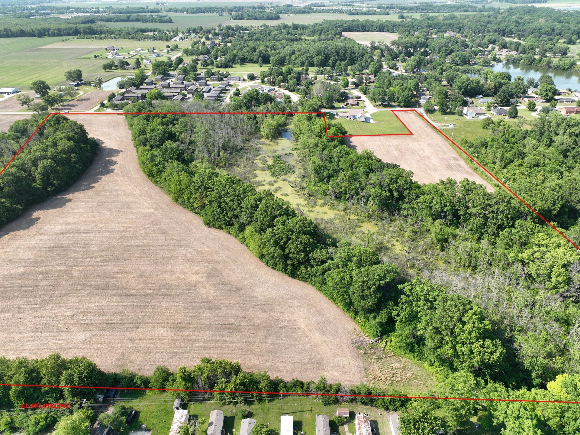 Aerial view of farmland with a tree-lined field, houses, and open fields in the distance.