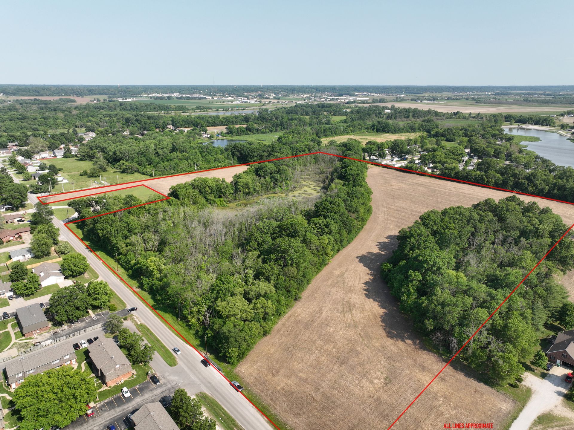 Aerial view of a wooded vacant lot bordered by roads and homes in a suburban area.