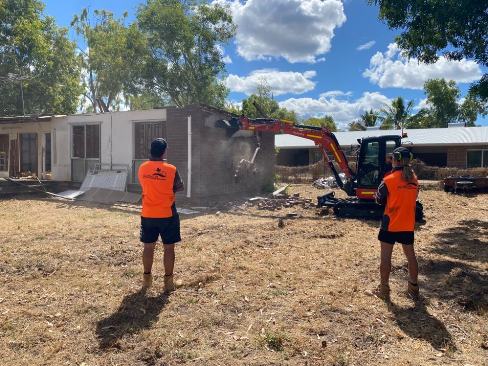 Two men are standing in front of a building being demolished by an excavator — Local Builders in Yarrawonga, NT