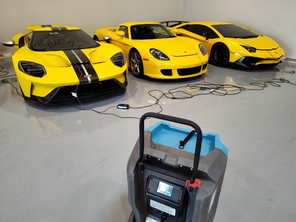 Three yellow sports cars are parked in a garage next to a vacuum cleaner.