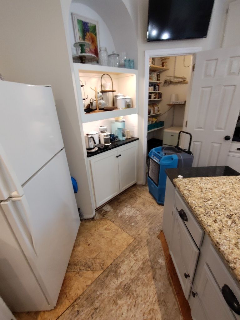 A kitchen with a refrigerator , sink , cabinets and a television.