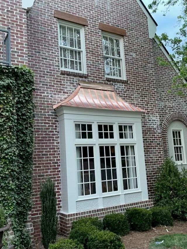 A brick house with a large window and a copper roof.