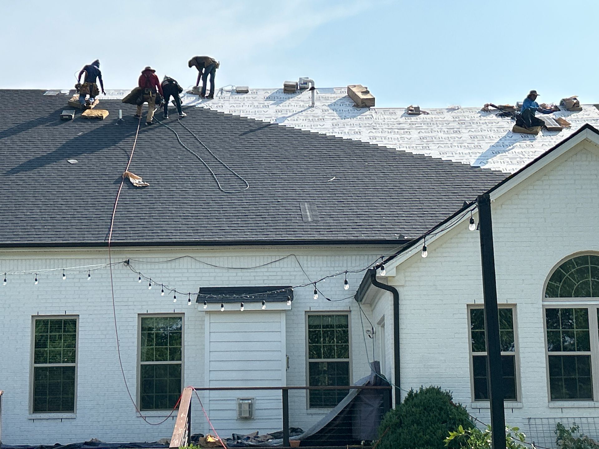 A group of people are working on the roof of a white house.