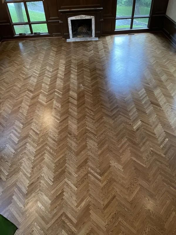 Empty room with glossy herringbone wood floor and a small fireplace at the far wall.