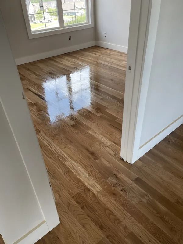 Empty room with glossy hardwood floors and large window, viewed through a doorway