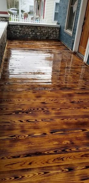 Wet wooden porch with a glossy finish, stone wall at the end, and a white chair by the doorway.