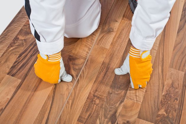Person in white pants and orange gloves working on a wooden floor with small white floor protectors