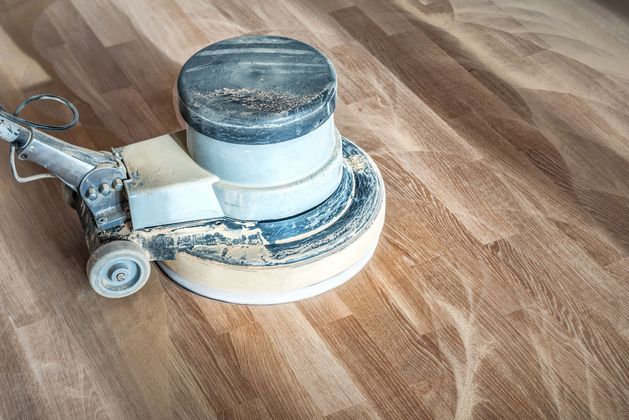 Floor buffer machine on a wood floor, showing its wheels and circular sanding pad