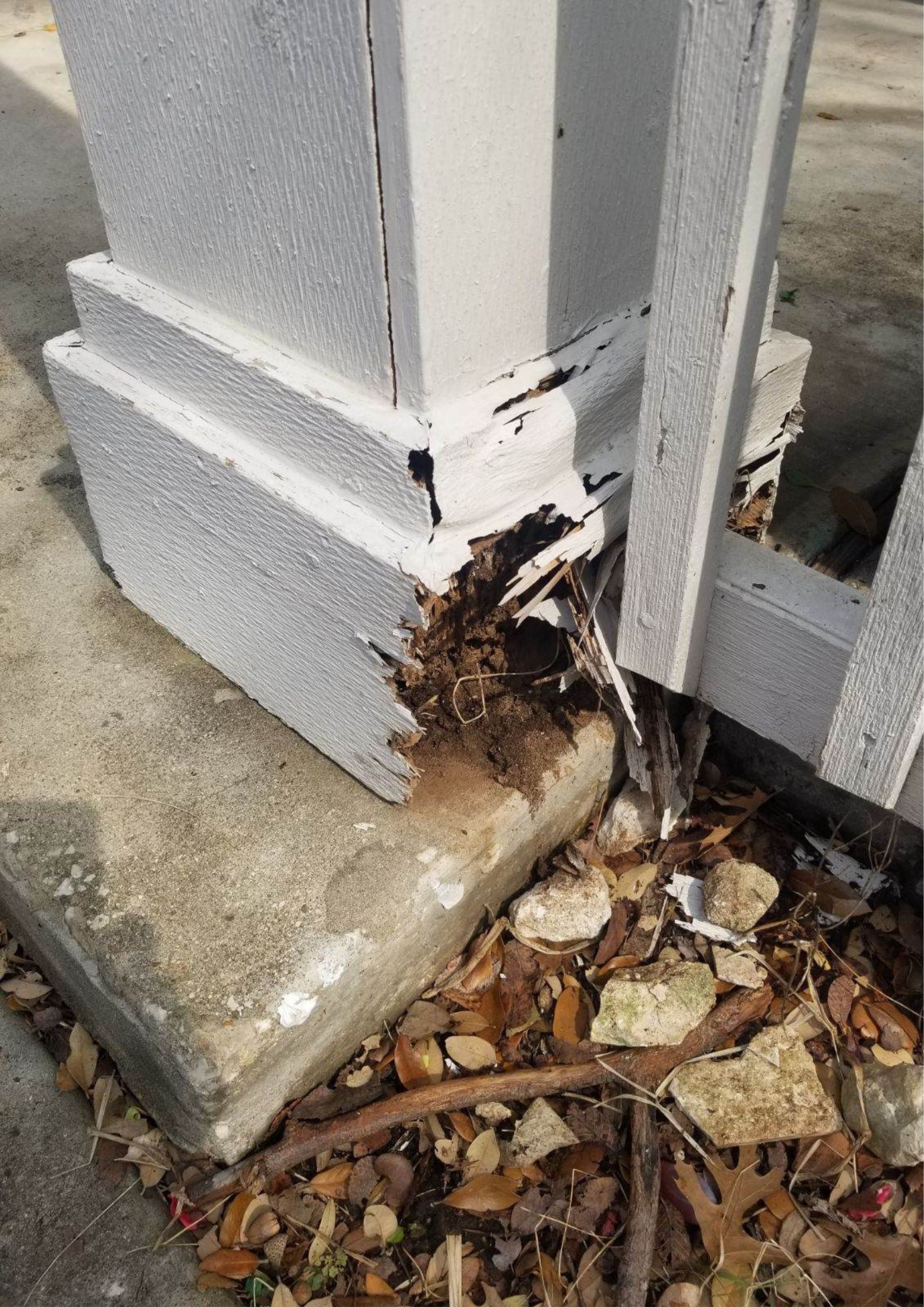 A pillar with a hole in it is sitting on the ground next to a fence.