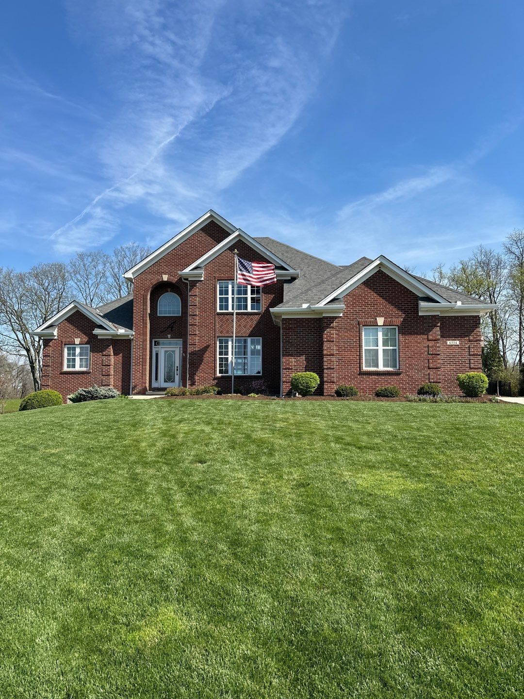 Brick suburban house with a large green lawn under a blue sky
