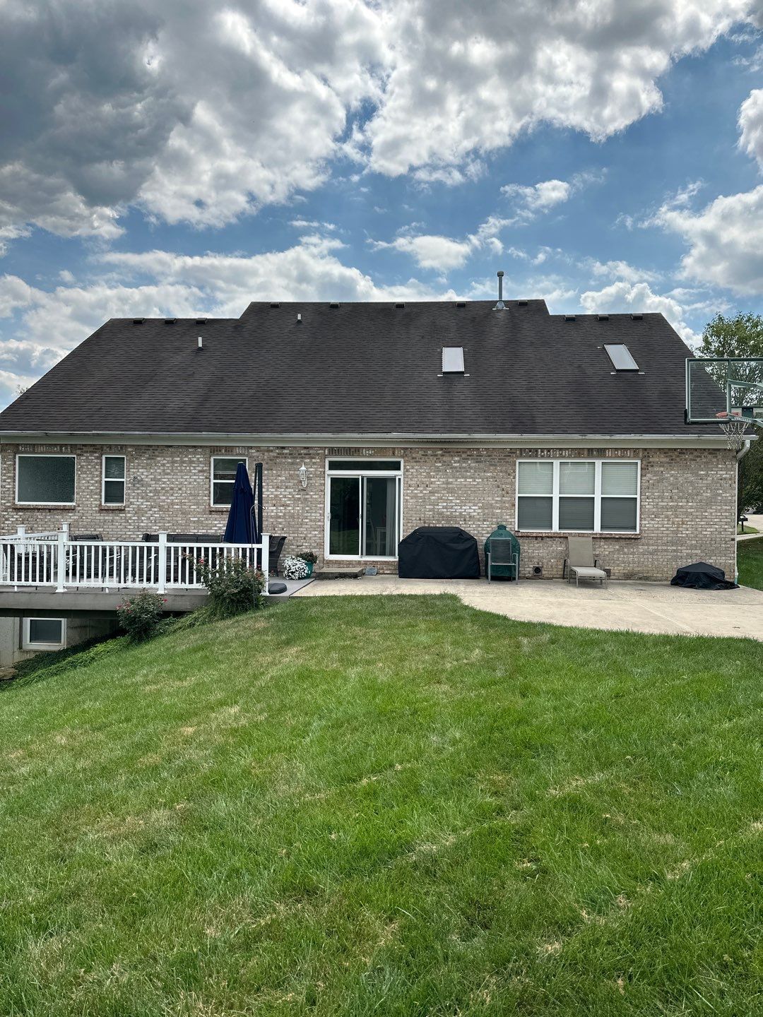Backyard view of a brick house with a sloped roof, patio furniture, and a grassy lawn under a cloudy sky