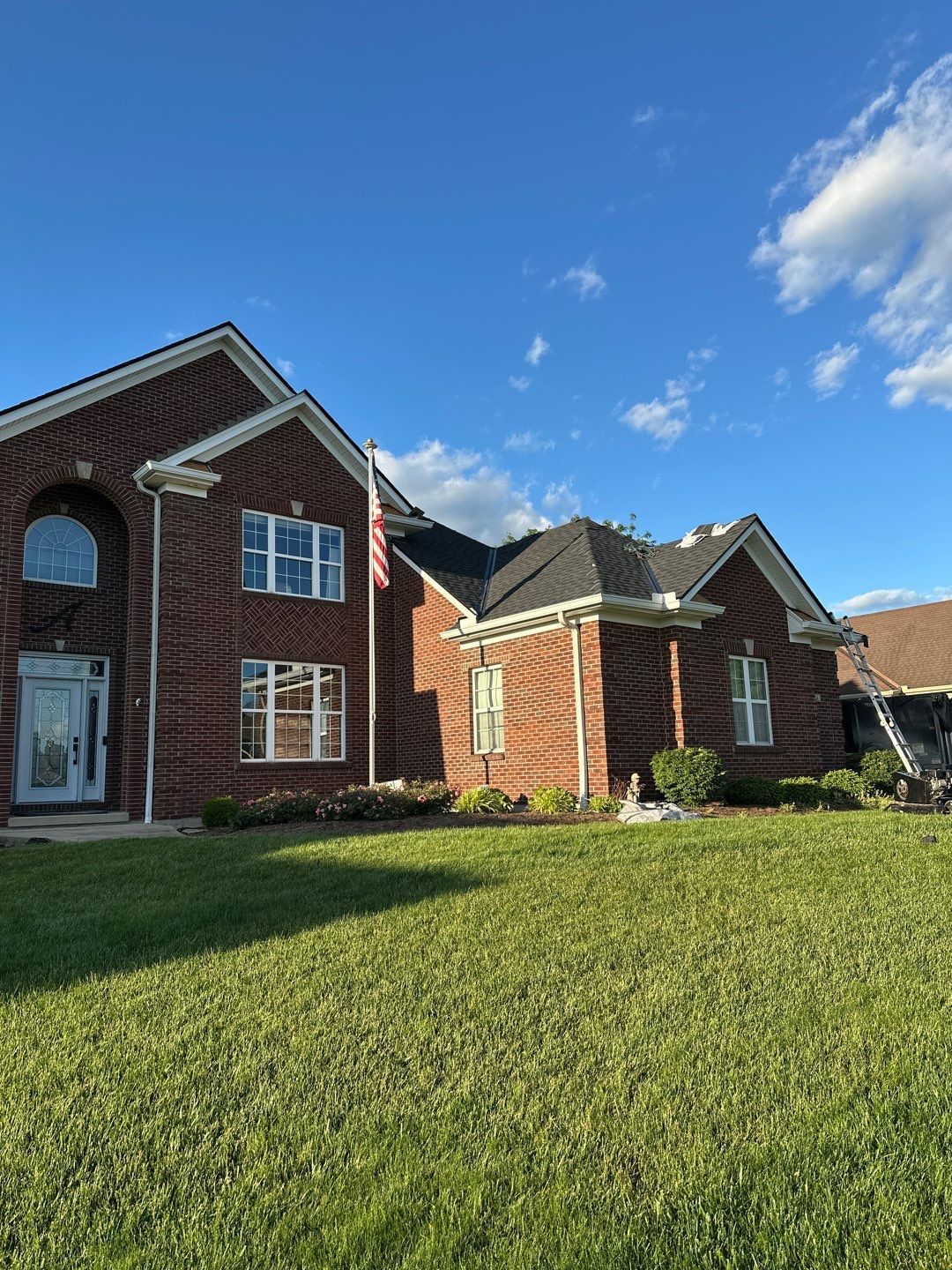 Brick suburban house with white trim and large green lawn under a blue sky