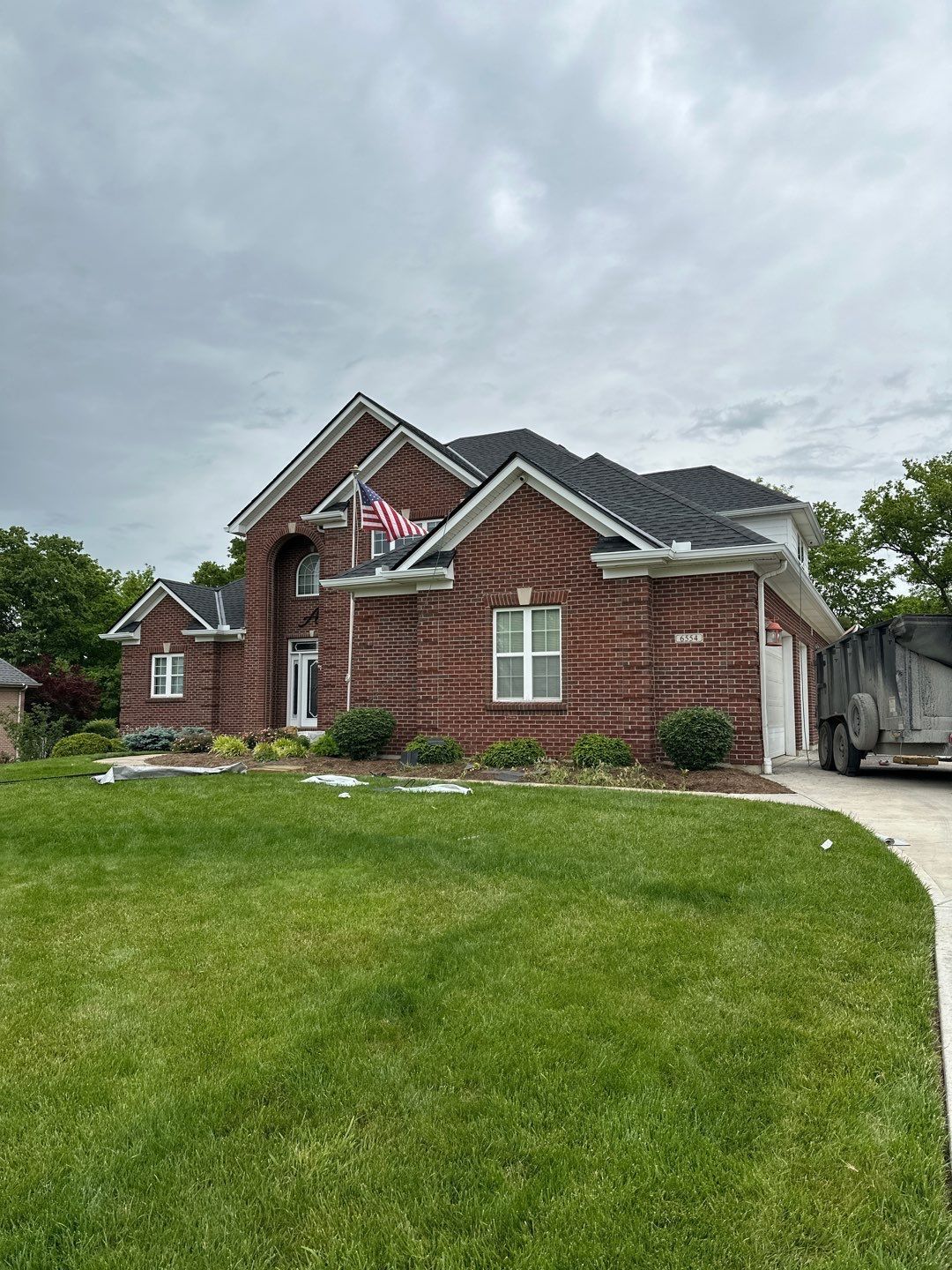 Brick suburban house with arched entry, two-car garage, and a green front lawn under cloudy skies