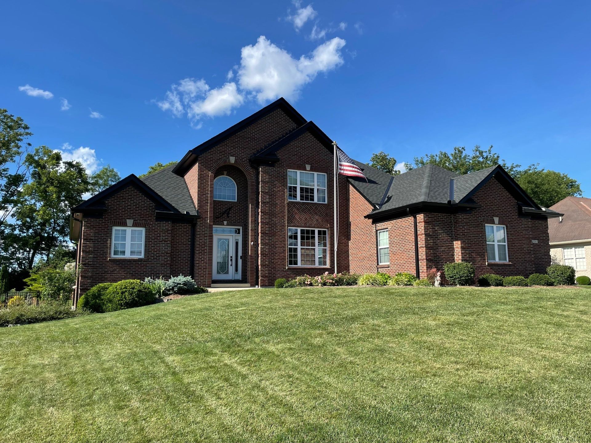 Brick suburban house with black roof, centered on a grassy lawn under a blue sky